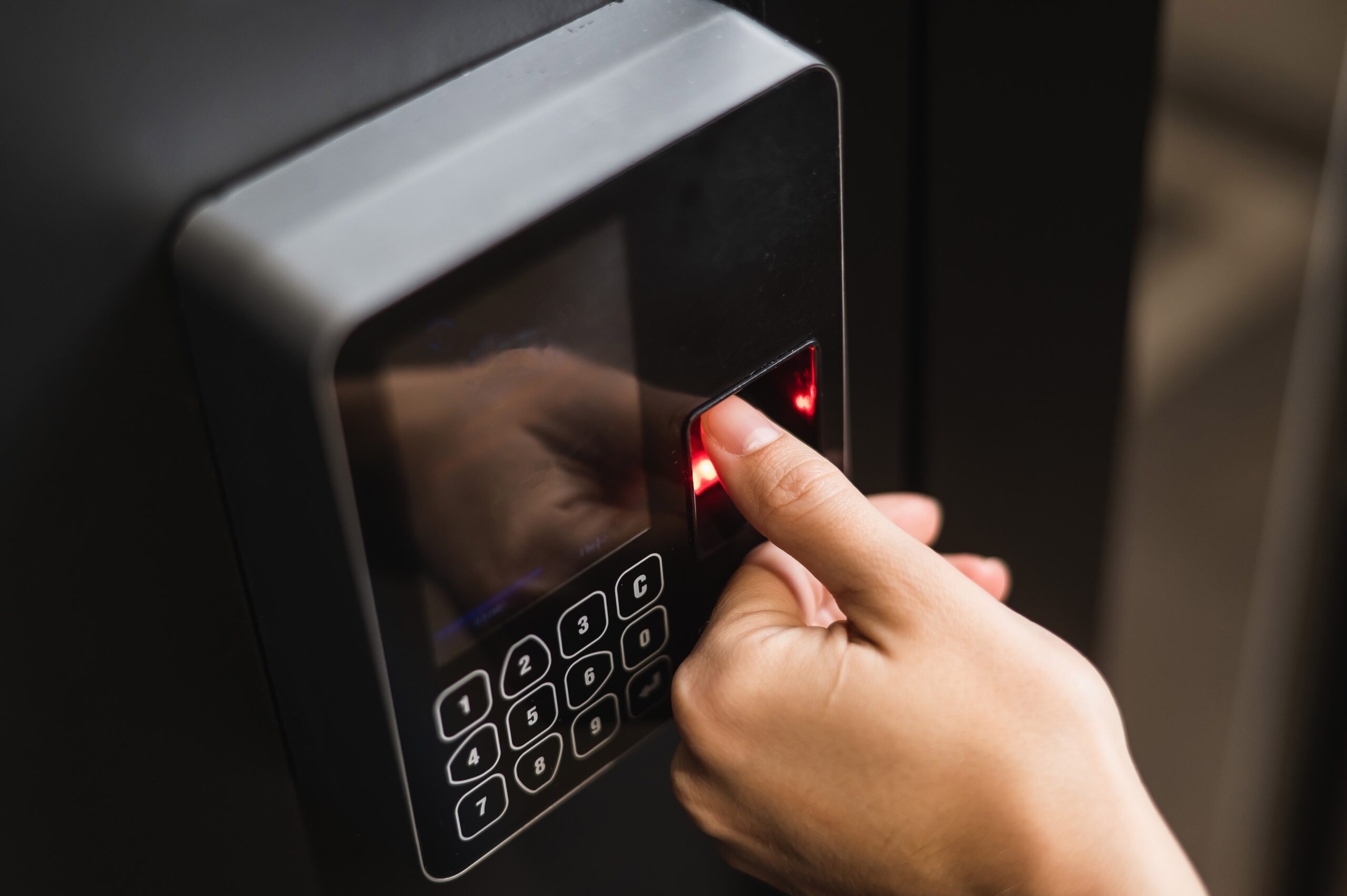 A person places their finger on a fingerprint scanner of an electronic device with a numeric keypad.